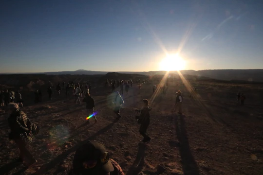 A group of families carrying belongings, walking through a rugged landscape at dusk.