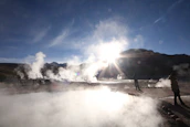 Engineers examining geothermal plant equipment amid steam vents in a rugged landscape.