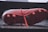 A close-up view of the underside of a red soccer cleat, resting on a reflective surface. The cleat features several studs for grip and a visible swoosh logo on the side. The laces are also visible, laid untied on the surface.