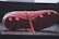 A close-up view of the underside of a red soccer cleat, resting on a reflective surface. The cleat features several studs for grip and a visible swoosh logo on the side. The laces are also visible, laid untied on the surface.