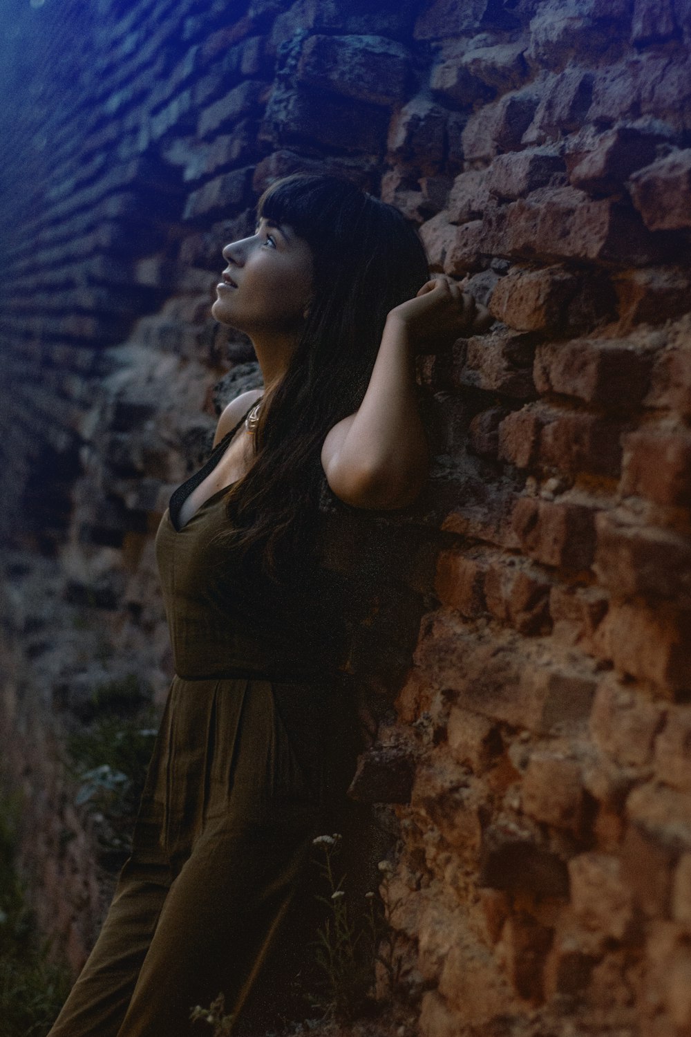 Femme portant un pantalon barboteuse sans manches marron appuyée sur un mur de briques