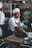 person in white top with gray apron holding pot