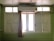 A set of white wooden window shutters with glass panels at the top. An air conditioning unit is mounted above the windows. A beige curtain is partially drawn to the side. The room has pale green walls made of horizontal panels.