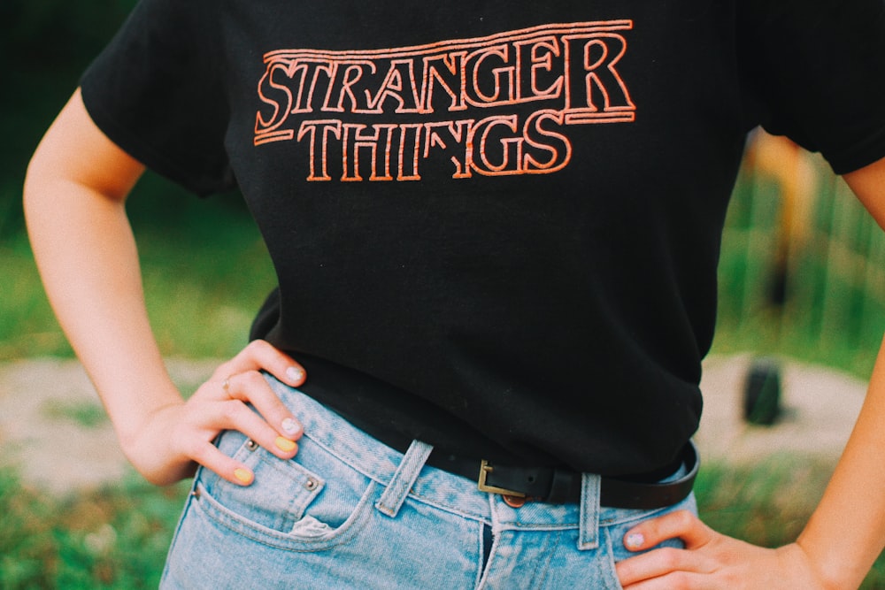 person wearing black and red stranger things print shirt standing with both arms akimbo
