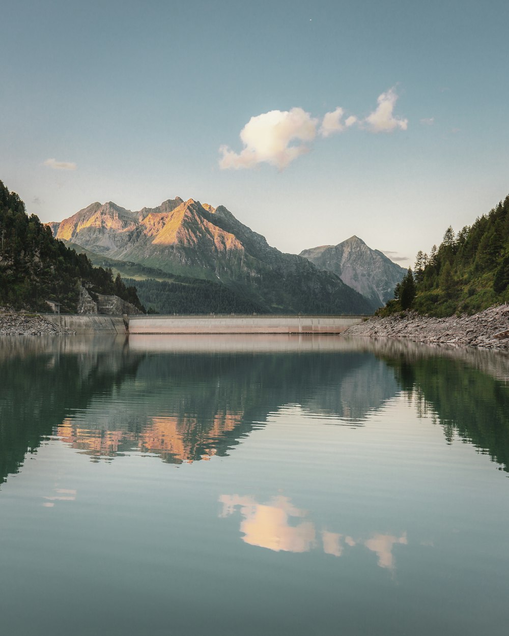 body of water near mountain under white clouds and blue sky during daytime