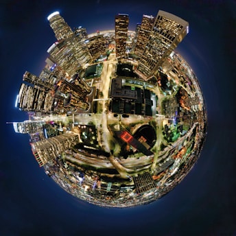 A spherical, panoramic view of a vibrant cityscape at night. Tall skyscrapers with illuminated windows are clustered on one side, creating an urban jungle. Streets with moving vehicles form bright lines and curves, while the city lights create a striking pattern against the dark sky.