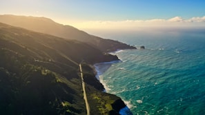 Aerial view of a winding coastline bathed in golden light with gentle waves meeting lush green cliffs.