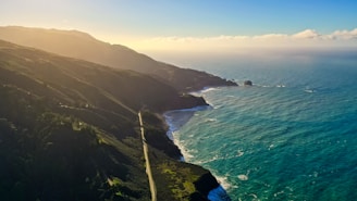Aerial view of a winding coastline bathed in golden light with gentle waves meeting lush green cliffs.