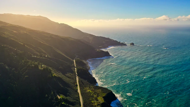A serene aerial view of a winding coastal road with cliffs and ocean under soft morning light.