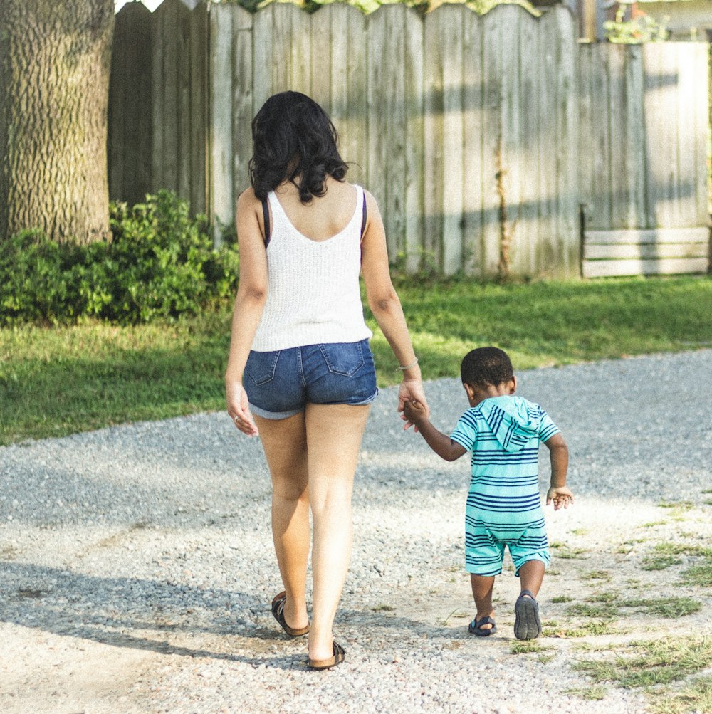 woman and boy holding hands walking near green grass at daytime
