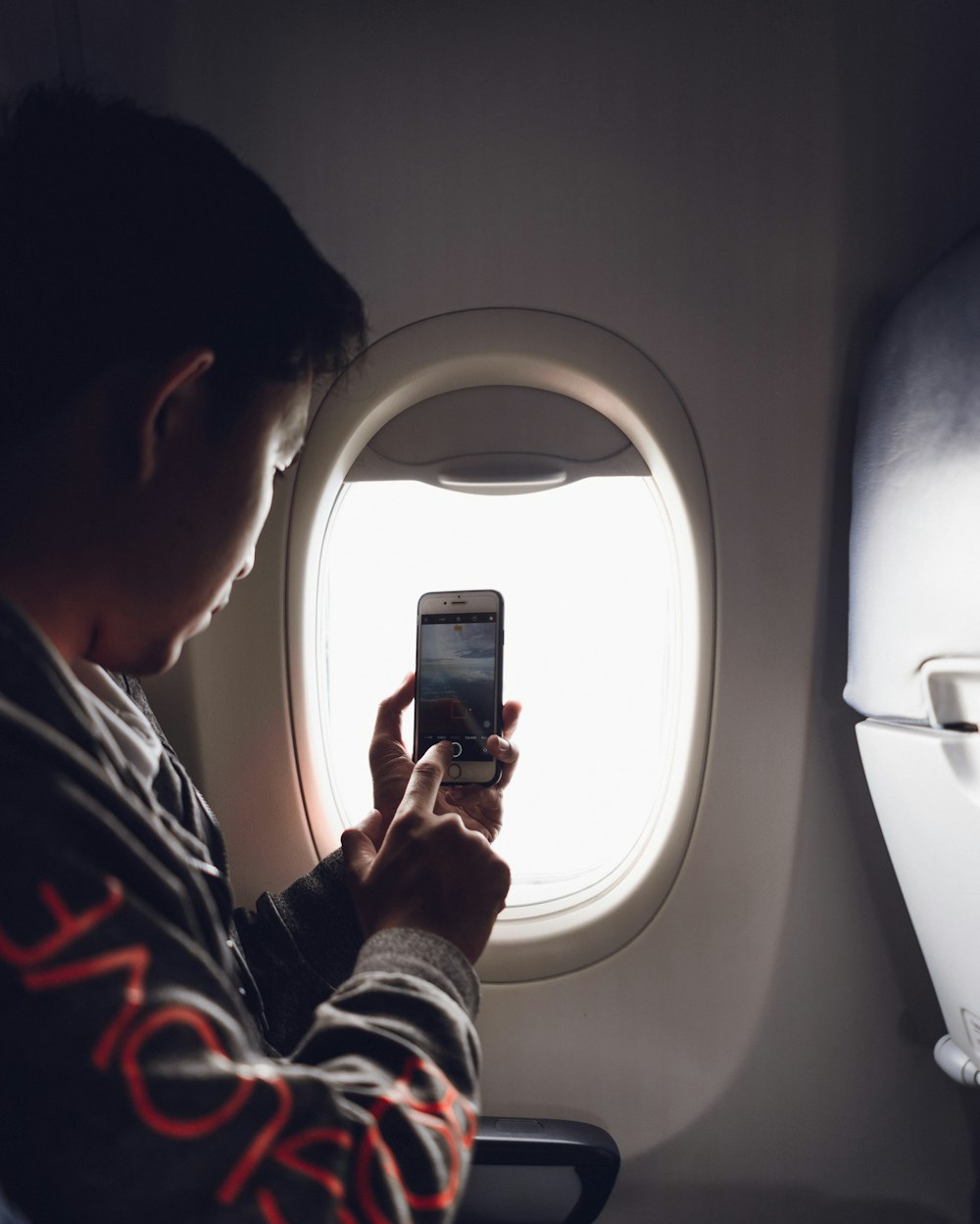 飛行機の窓のそばに座ってスマートフォンを使う男性