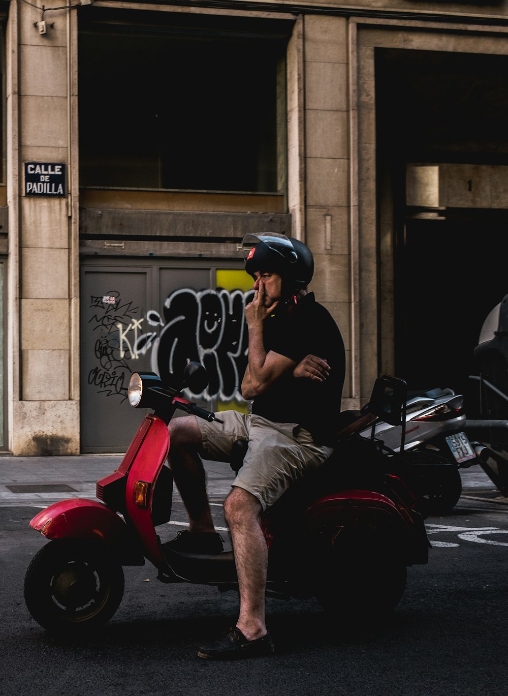 man wearing black shirt sitting on red motor scooter