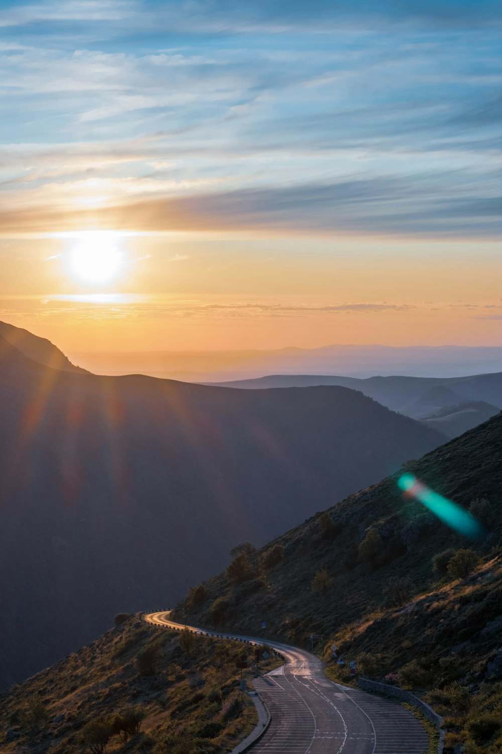 the sun is setting over a winding mountain road