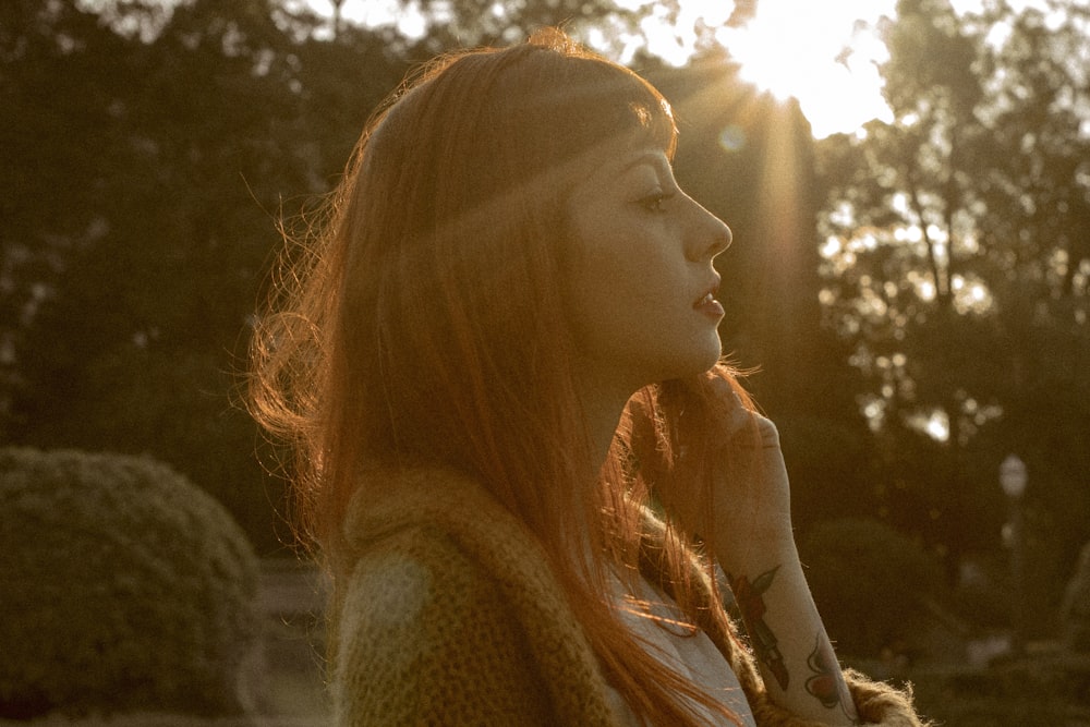 a woman standing in a park with the sun behind her