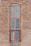A tall, narrow window with a red frame set into a brick wall. The window is composed of multiple small square panes of glass, arranged in a grid pattern, typical of old or historic buildings.