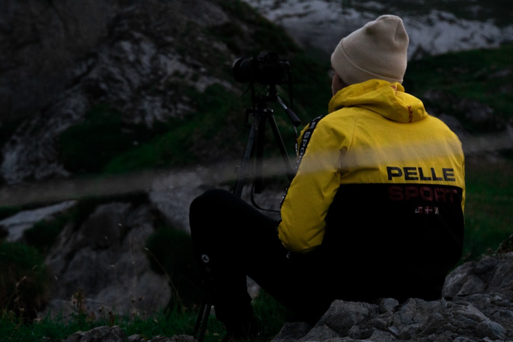 uma pessoa sentada em uma rocha com uma câmera