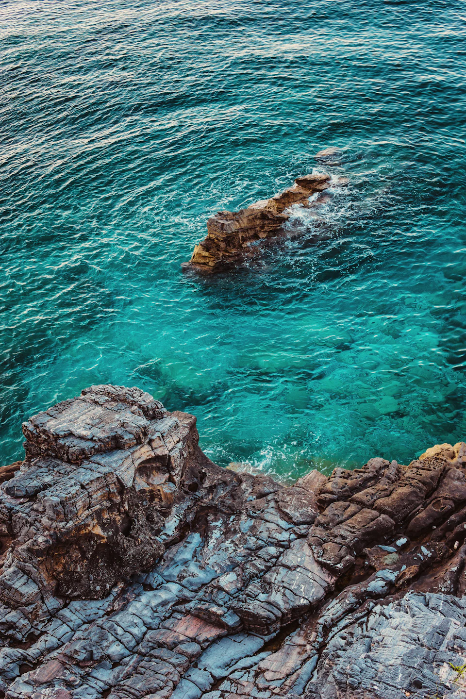 Rocky cliff with jagged rocks overlooking deep blue ocean and small island in distance