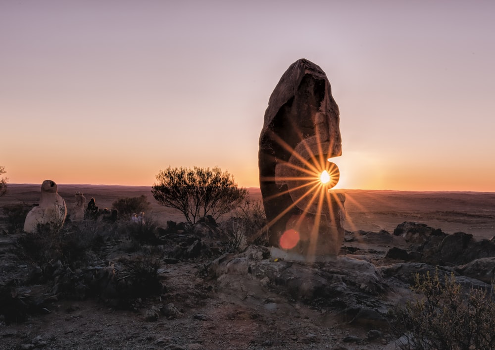 the sun is setting behind a large rock in the desert
