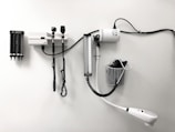 Medical equipment is neatly mounted on a white wall, including an otoscope, an ophthalmoscope, a sphygmomanometer, and a thermometer. The layout suggests a clinical setting likely intended for patient examination.