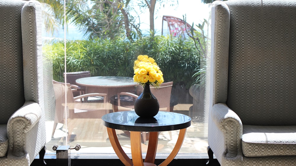 a vase with yellow flowers sitting on a table in front of a window