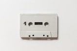 A vintage audio cassette tape featuring a simple, minimalistic design with a white casing. It is labeled with 'Side 1' and includes standard features such as twin reels, a small window to view the tape, and recording label markings.