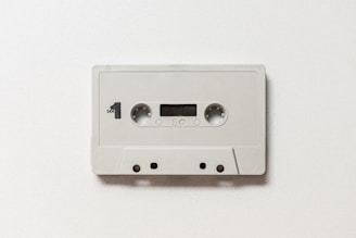 A vintage audio cassette tape featuring a simple, minimalistic design with a white casing. It is labeled with 'Side 1' and includes standard features such as twin reels, a small window to view the tape, and recording label markings.