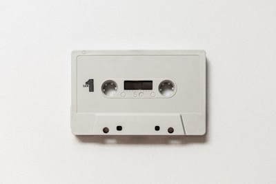 A vintage audio cassette tape featuring a simple, minimalistic design with a white casing. It is labeled with 'Side 1' and includes standard features such as twin reels, a small window to view the tape, and recording label markings.
