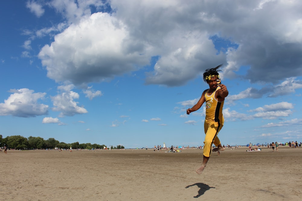 man wearing yellow-and-black tracksuit about to jump on brown sand