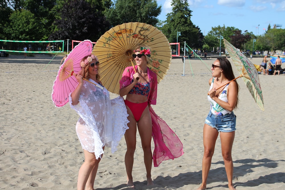 three women on beach holding umbrellas