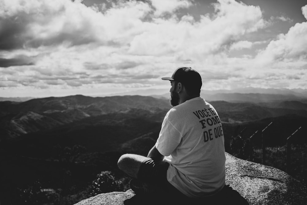 greyscale photography of man sitting on rock