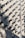 A wall covered in numerous surveillance cameras, all aligned in neat rows and columns. The arrangement creates a pattern against the light-colored brick wall, casting strong shadows that add a sense of repetition and uniformity.