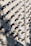 A wall covered in numerous surveillance cameras, all aligned in neat rows and columns. The arrangement creates a pattern against the light-colored brick wall, casting strong shadows that add a sense of repetition and uniformity.