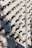 A wall covered in numerous surveillance cameras, all aligned in neat rows and columns. The arrangement creates a pattern against the light-colored brick wall, casting strong shadows that add a sense of repetition and uniformity.