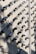 A wall covered in numerous surveillance cameras, all aligned in neat rows and columns. The arrangement creates a pattern against the light-colored brick wall, casting strong shadows that add a sense of repetition and uniformity.