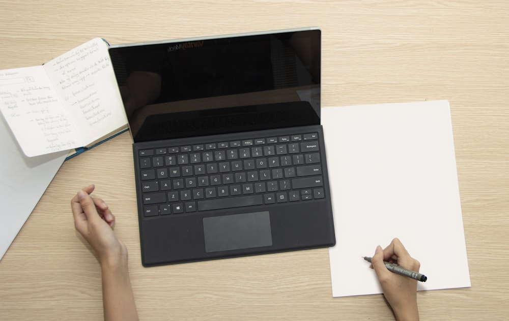 a person writing on a piece of paper next to a laptop