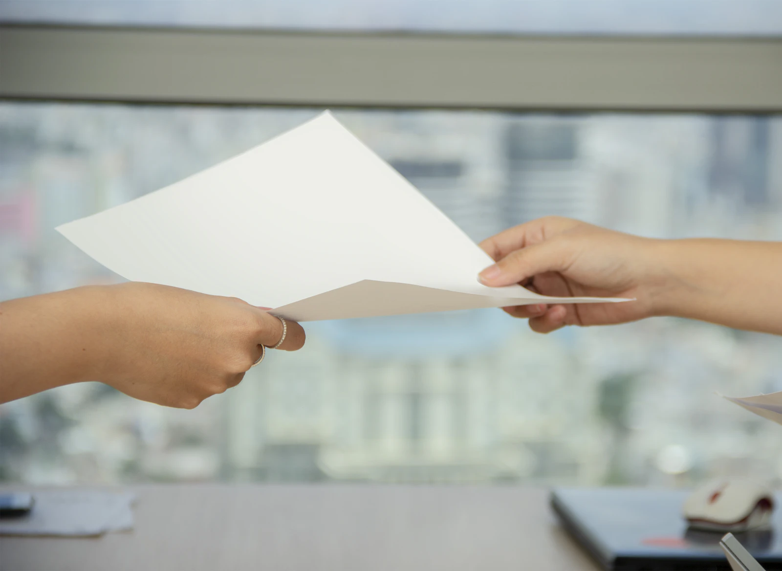 One person handing a sheet of paper to another in front of a bright window