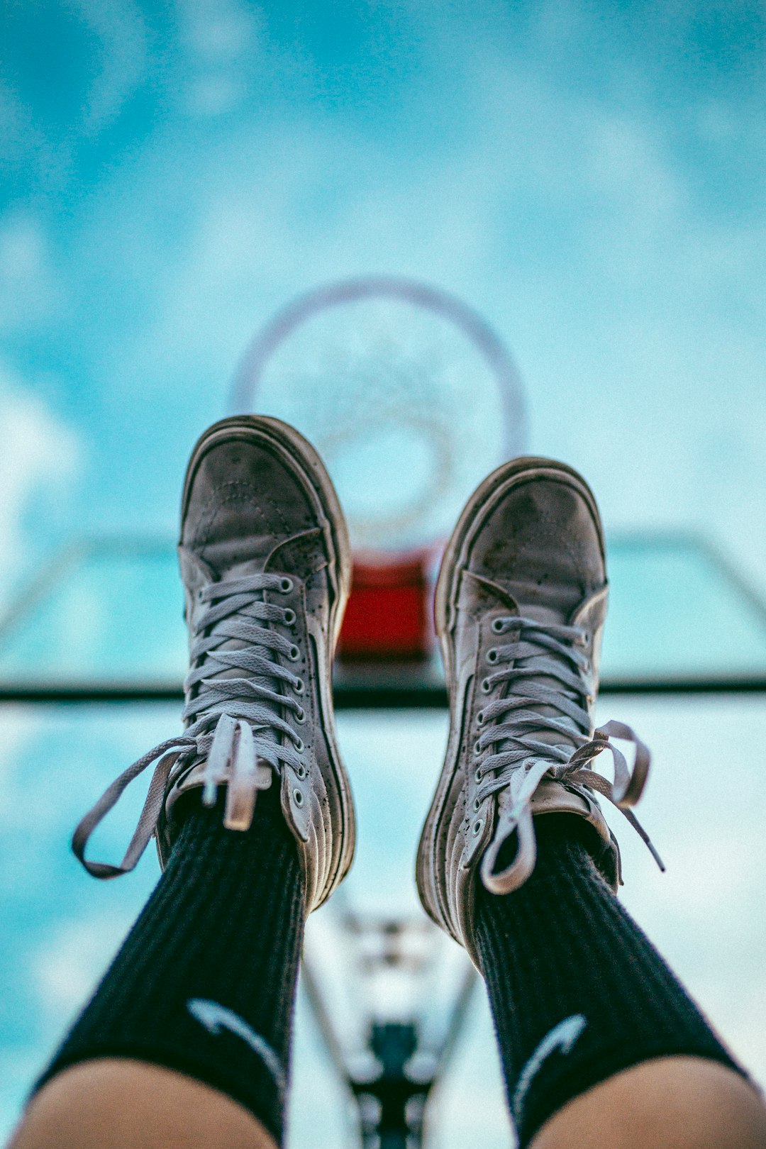 feet with dirty white basketball shoes raised into air under basketball hoop