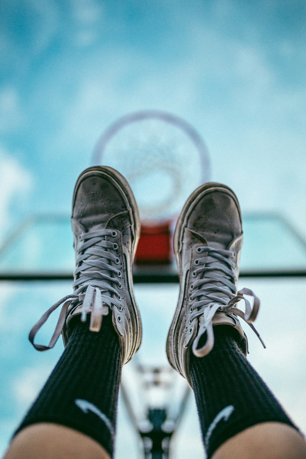 feet with dirty white basketball shoes raised into air under basketball hoop
