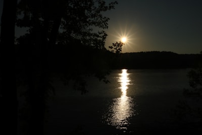 A peaceful sunset over a calm lake with silhouettes of trees.