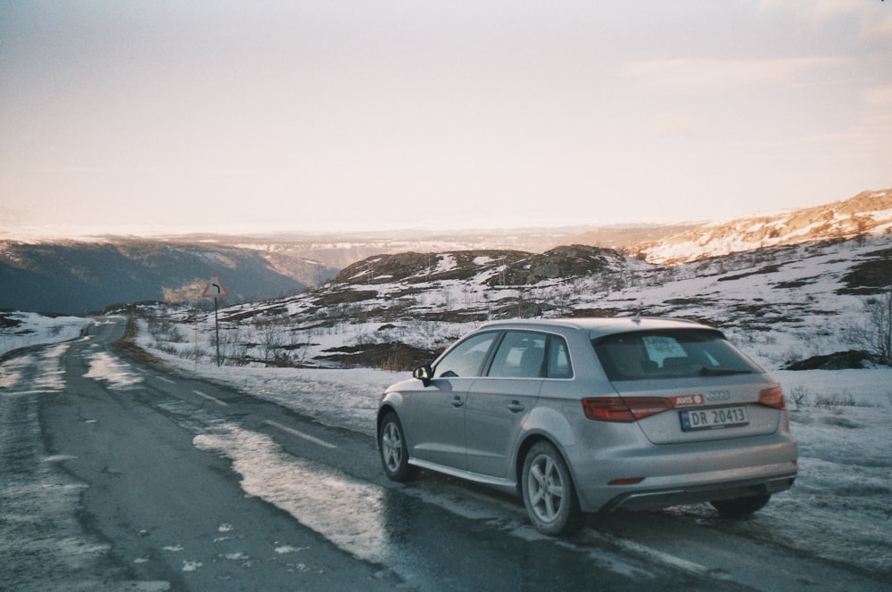 hatchback cinza de 5 portas na estrada perto do campo coberto de neve