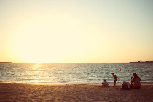 three people sitting near seashore during daytime