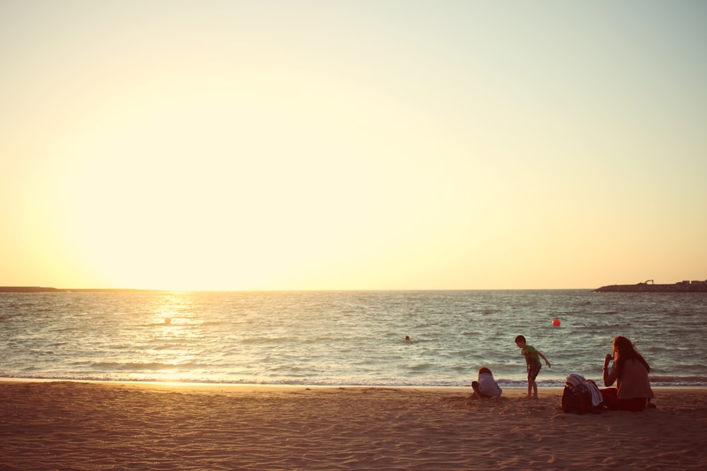 three people sitting near seashore during daytime