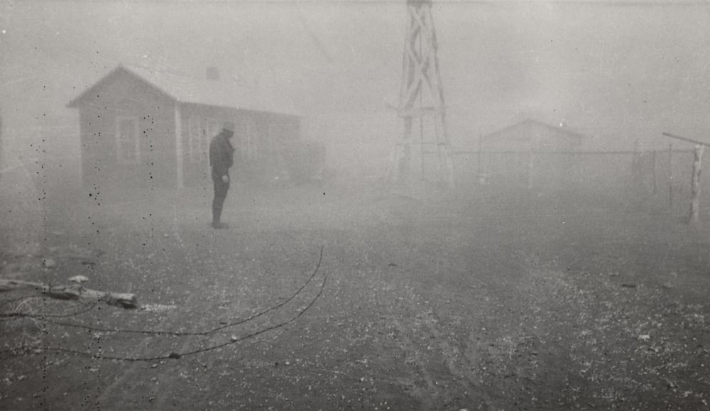 Fotografía en escala de grises de un hombre de pie cerca de la casa