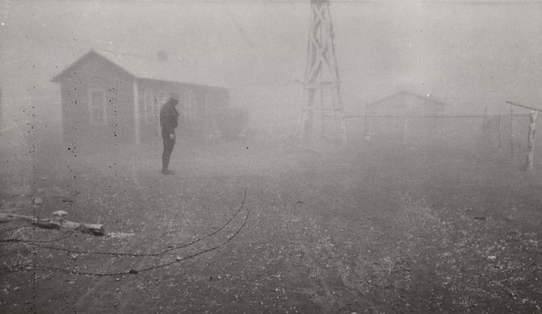 grayscale photography of man standing near house