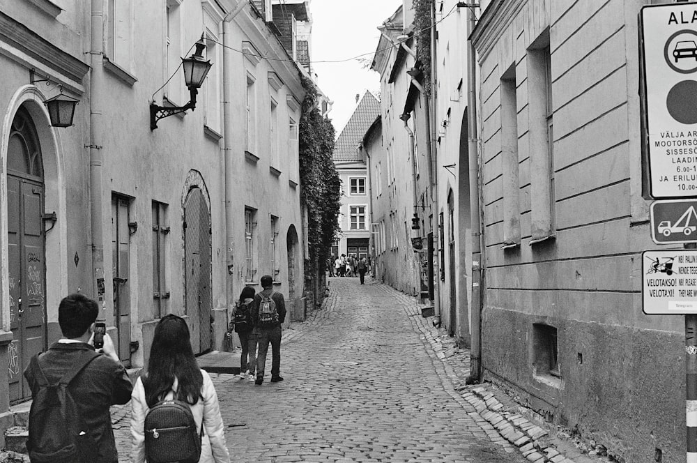 grayscale photography of people walking near road beside buildings