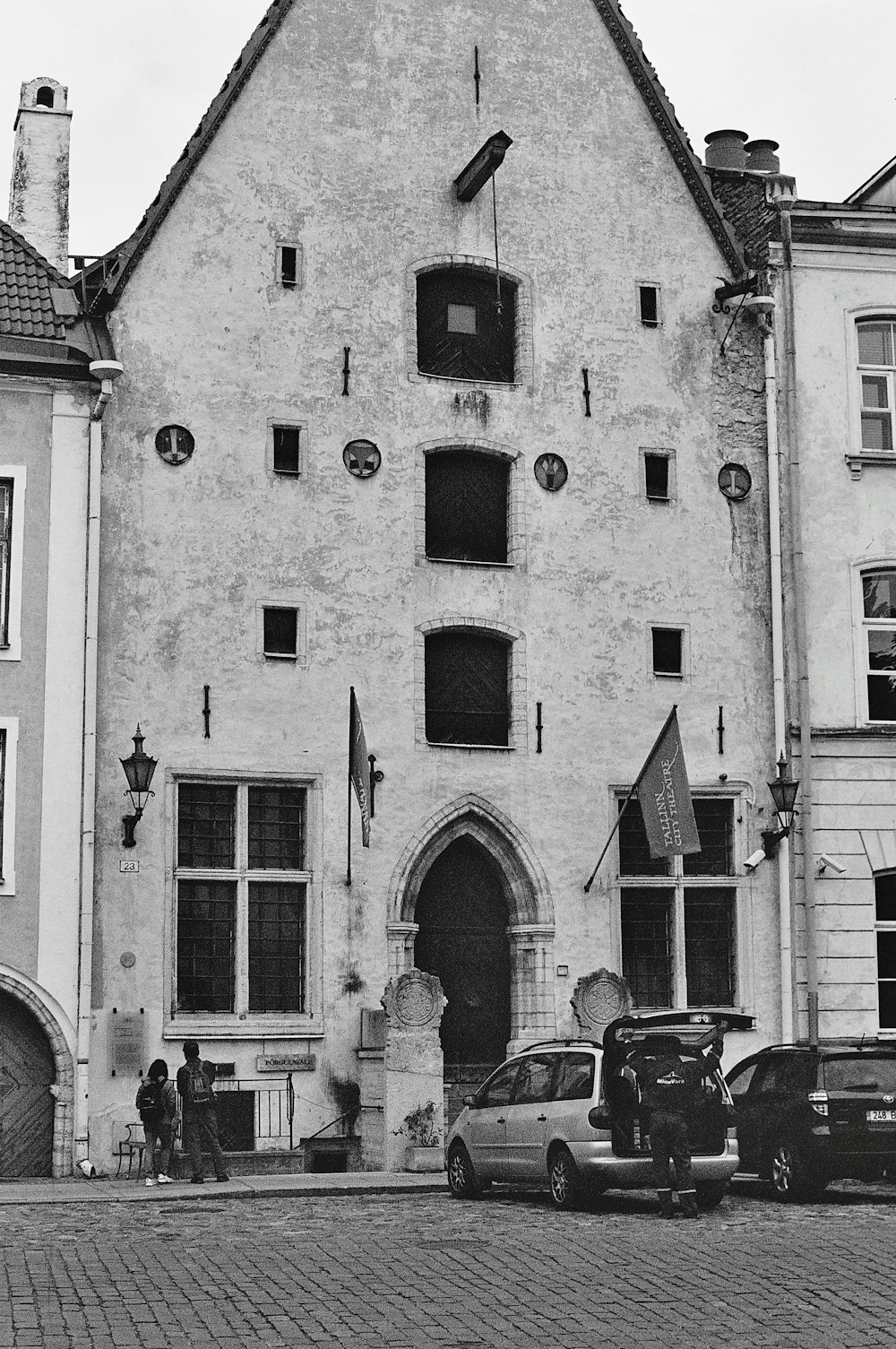 grayscale photography of people and vehicles near building