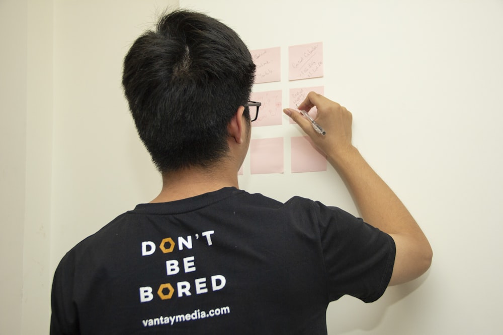 man wearing black and white t-shirt standing while writing on pink sticky notes