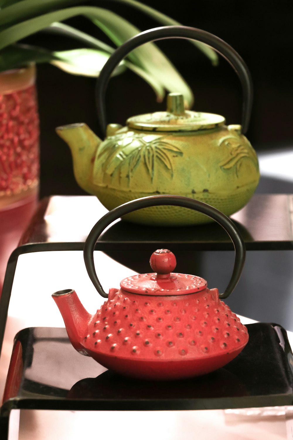 two red and green teapots on black shelf