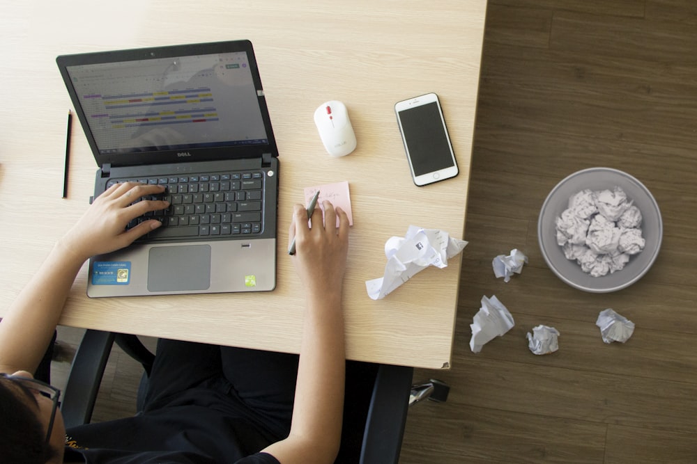 person using laptop and holding pen and smartphone and mouse on table