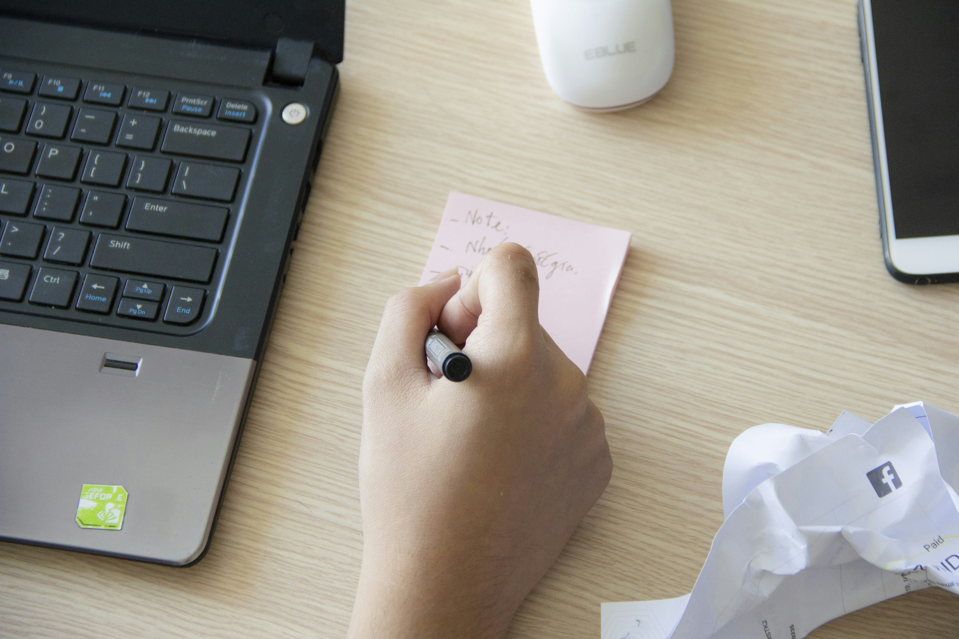 person writing on sticky note beside laptop